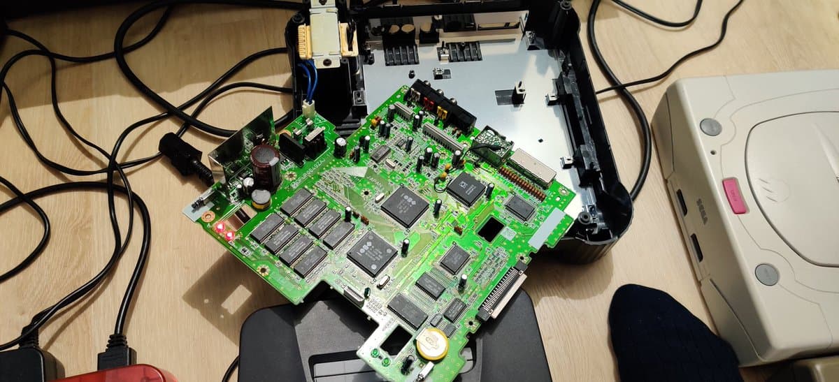 Panasonic FZ-1 motherboard with green PCB, multiple RAM chips, and bridged power traces during restoration work on wooden desk.