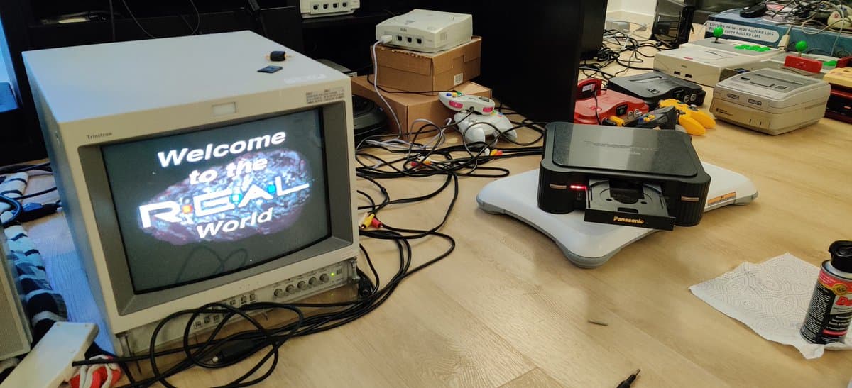 Panasonic FZ-1 3DO displaying "Welcome to the Real World" boot screen; Panasonic floppy drive and networking hardware on workbench during restoration.