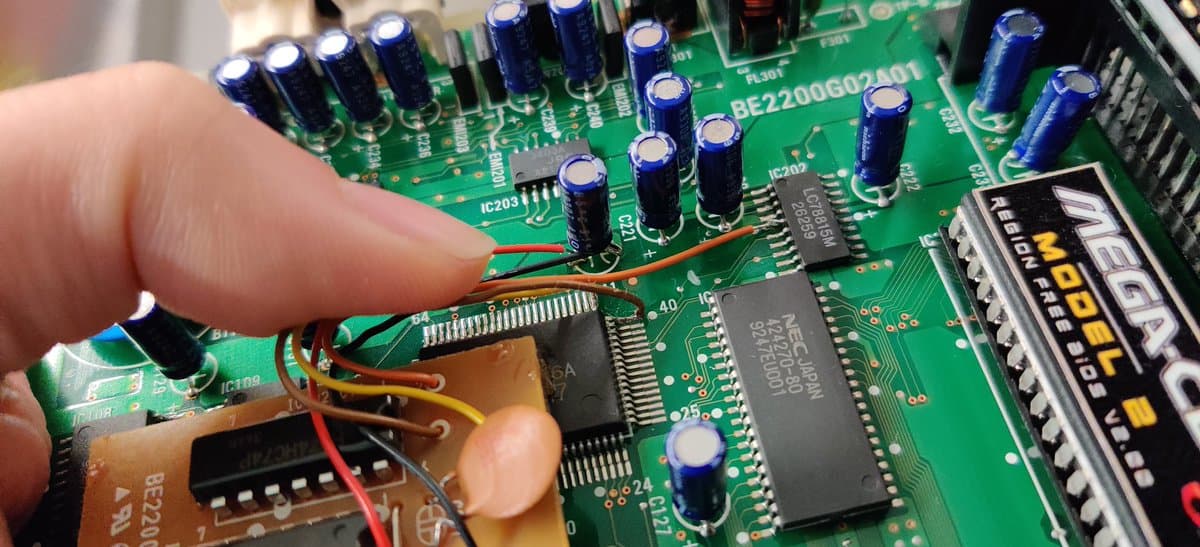 Sega Mega-CD 2 circuit board showing factory bodge wires soldered to capacitors during restoration inspection.