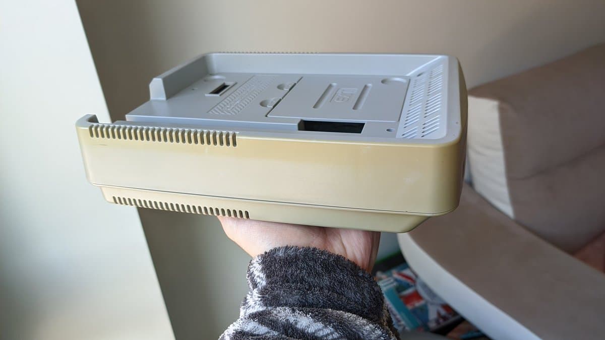 Hands holding a retrobrighted Nintendo SatellaView unit showing the cream-colored plastic shell and grey top panel with ventilation grilles.