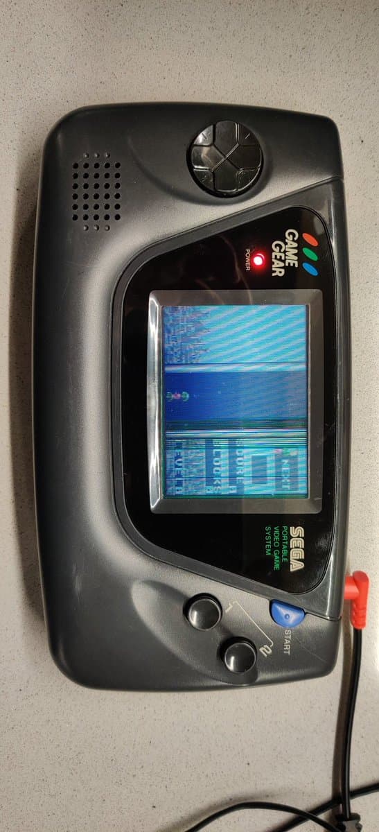 Sega Game Gear displaying horizontal line artifacts on screen; console boots and plays audio but has defective display after electrolyte damage repair.