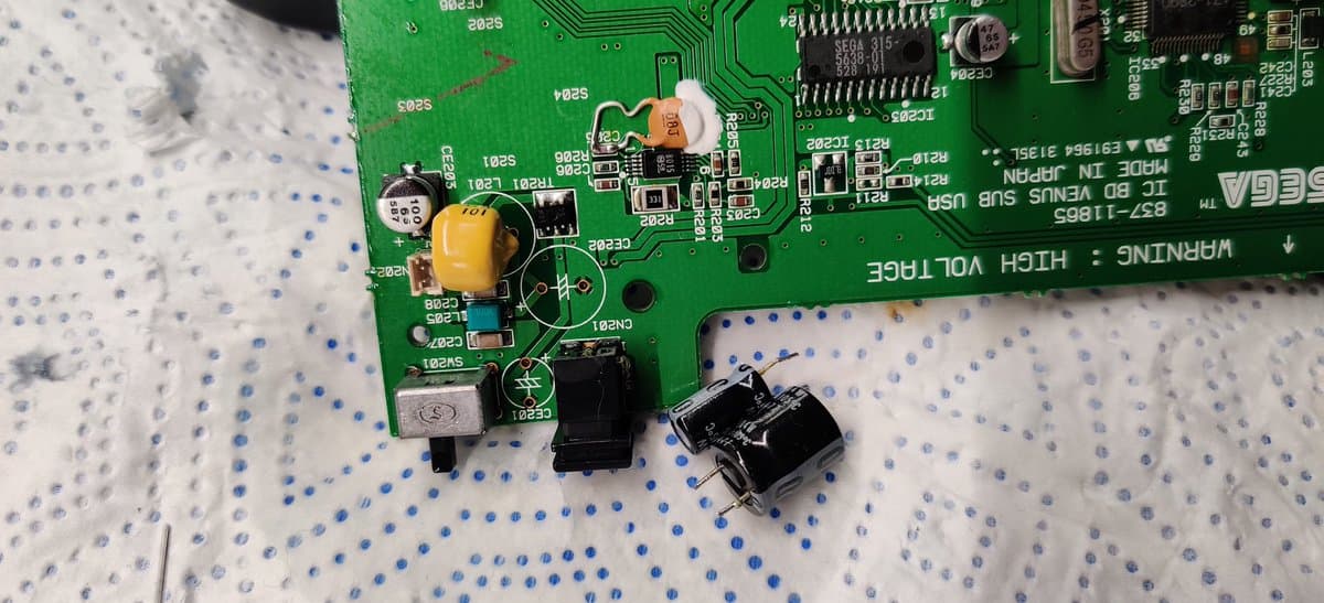 Sega Nomad motherboard showing replaced capacitors, cleaned solder joints around power section, and refurbished power jack during restoration.