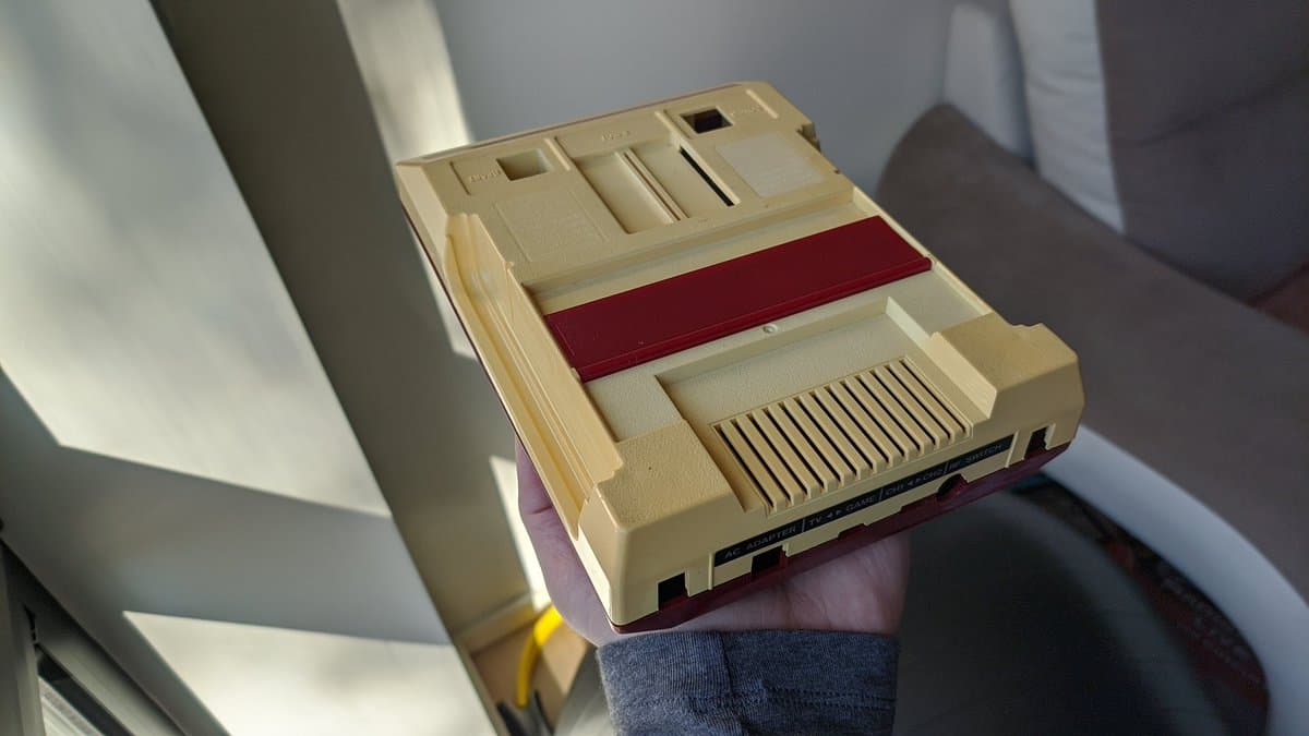 Cream-colored Famicom motherboard with red cartridge connector and composite mod board installed, displayed from top angle.