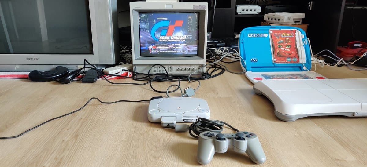 Sony PSOne console with controller on wooden workbench, Gran Turismo 4 displayed on CRT monitor, retro gaming setup.