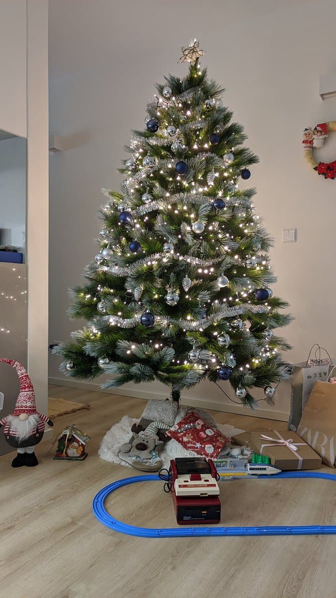 Modified Famicom with composite mod board and new stickers, displayed festively beneath illuminated Christmas tree with blue train track set.