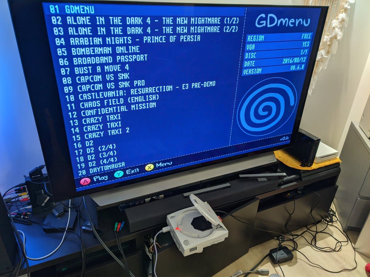 Sega Dreamcast VA0 connected to TV displaying GDmenu interface with game list; white GDEMU module visible below console.