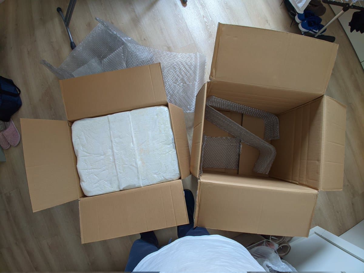 Two cardboard boxes open on wooden floor containing white foam padding and bubble wrap protective packaging for shipped Sony PVM-14M4J CRT monitor.