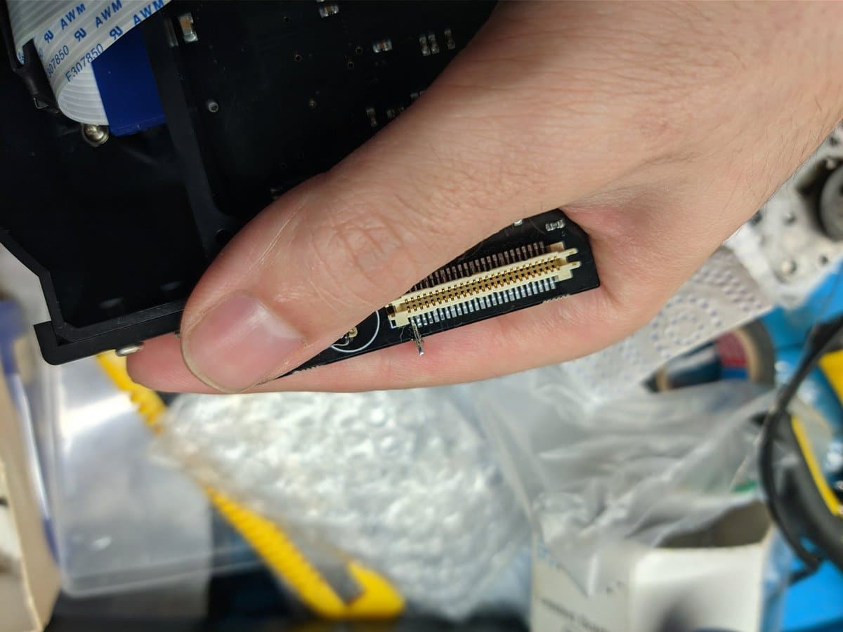 Close-up of GDEMU resistor mod installed on Dreamcast motherboard, showing dual gold-plated connector pins soldered to black PCB.