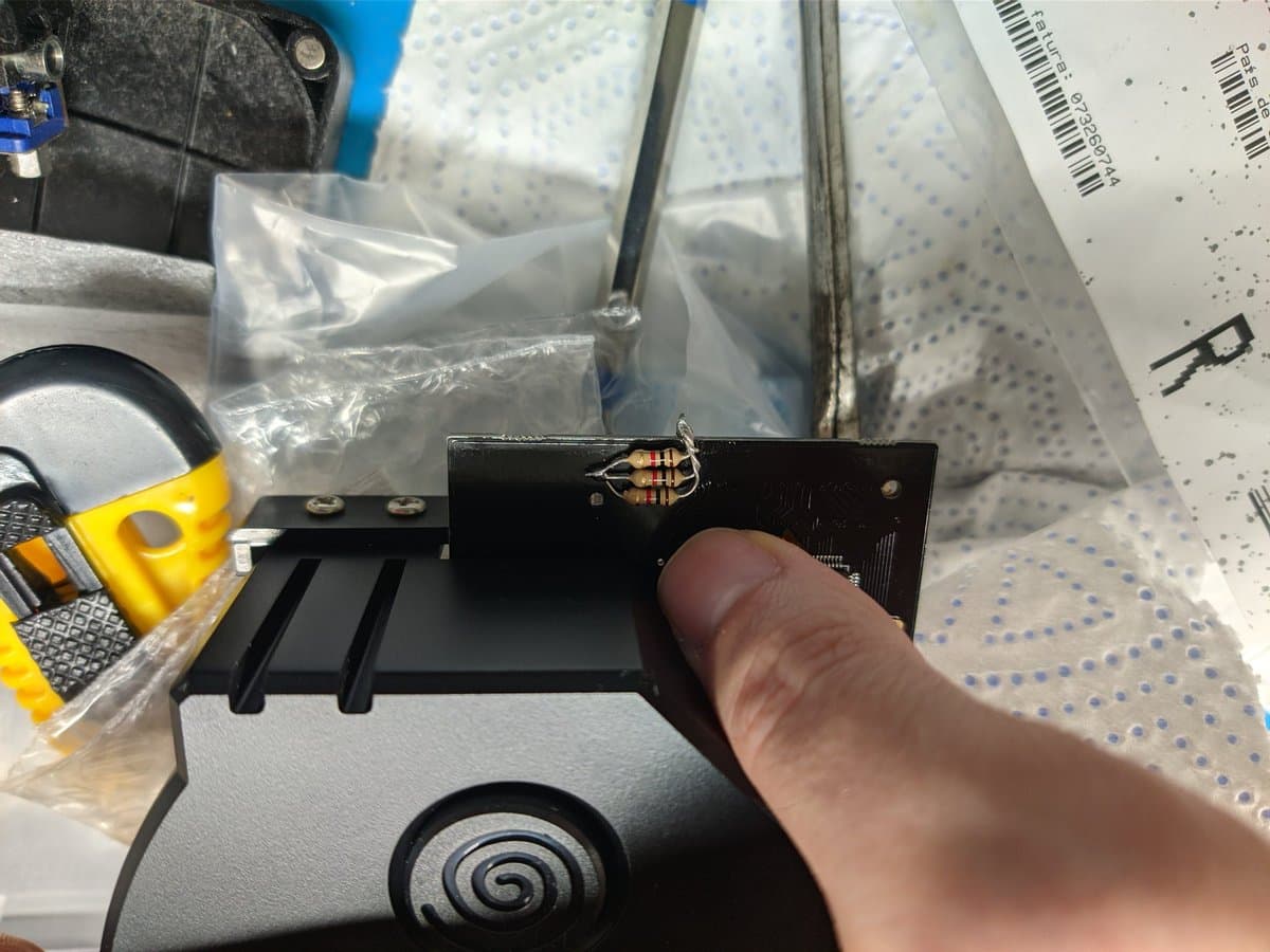 Close-up of GDEMU resistor mod installation on Dreamcast motherboard, finger pointing to soldered resistor component on black PCB section.