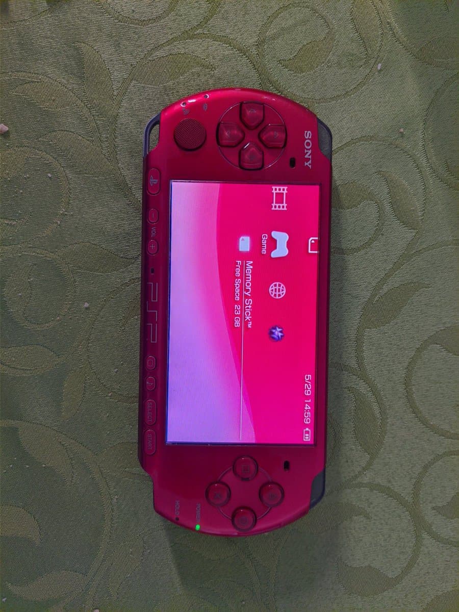 Red Sony PSP-3000 displaying memory stick menu on screen, showing 5:29/14:59 time stamp during battery replacement repair work.