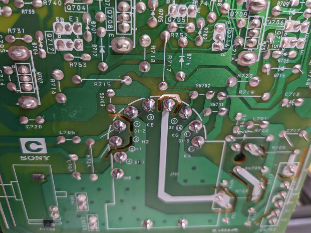 Close-up of Sony PVM-14M4J C board showing broken solder joint at KB tube pin with multimeter probe positioned for diagnosis.