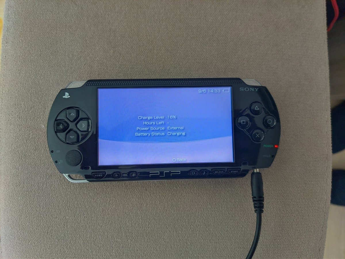 Sony PSP-1000 displaying battery status screen showing 16% charge level while charging via external power source.