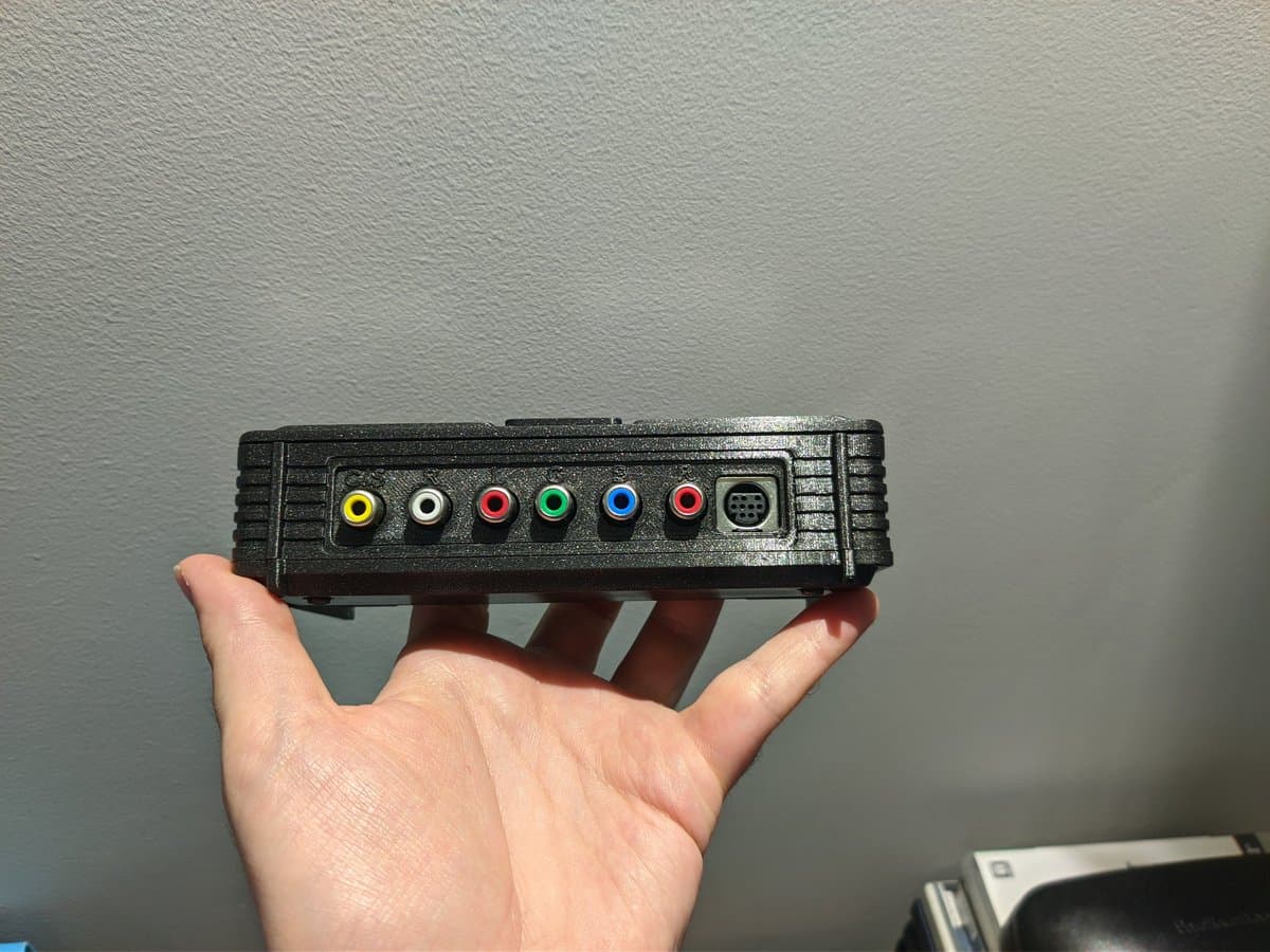 Hand holding NEC PC Engine AV adapter by PointerFunction featuring RCA connectors (yellow, white, red, green, blue, red) and DB-9 port.