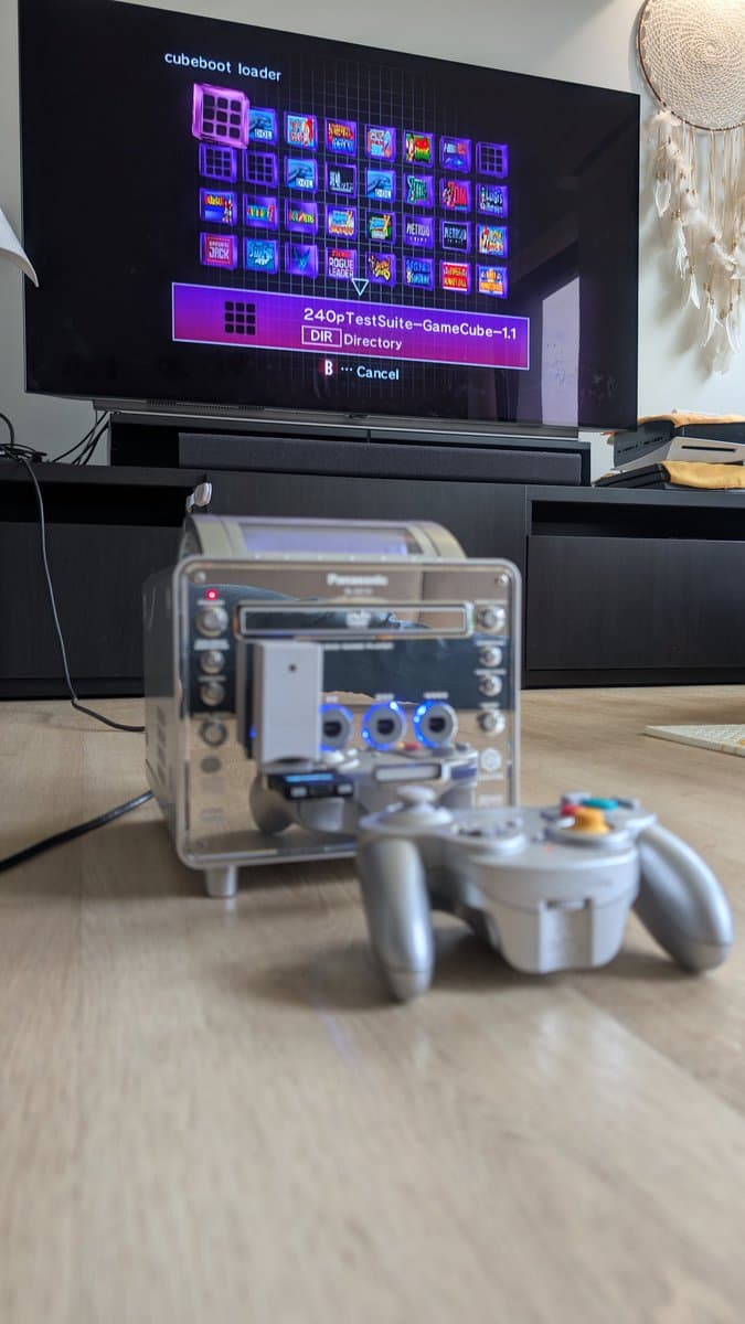 Panasonic Q with FlippyDrive installed displaying Cubeboot loader menu; GameCube controller and transparent drive housing visible on desk.