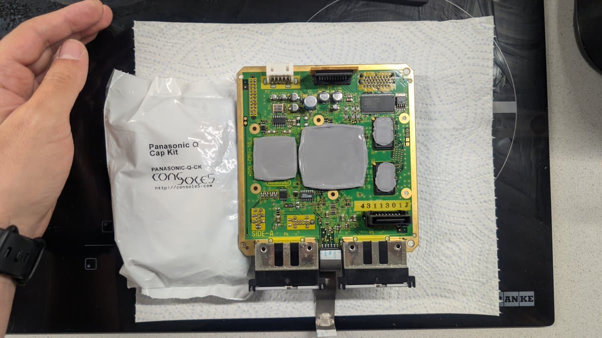 Panasonic Q motherboard being recapped, with fresh capacitors installed and Panasonic Q-CK cap kit visible in plastic bag to the left.