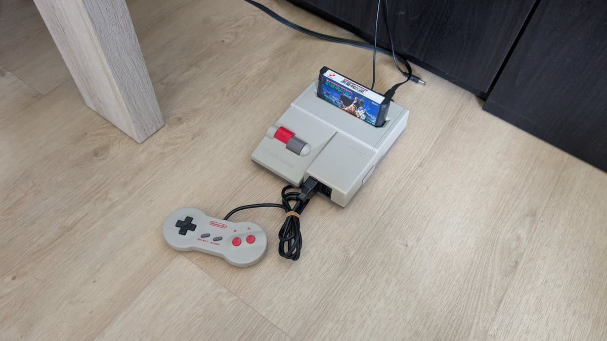 Nintendo AV Famicom on wooden floor with controller, showing cartridge slot cleaning and recap repair work in progress.