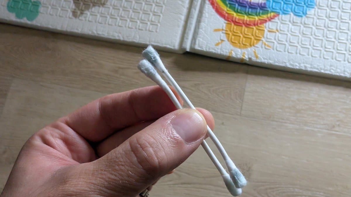 Two cotton swabs held in hand, tools used for cleaning oxidation from AV Famicom cartridge slot during repair.