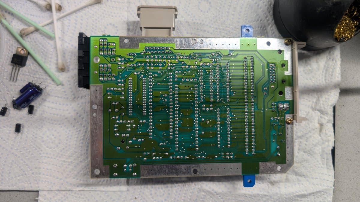 Nintendo AV Famicom main board after recap and cleaning, showing replaced capacitors, reflowed power jack pins, and organized component layout on white work surface.