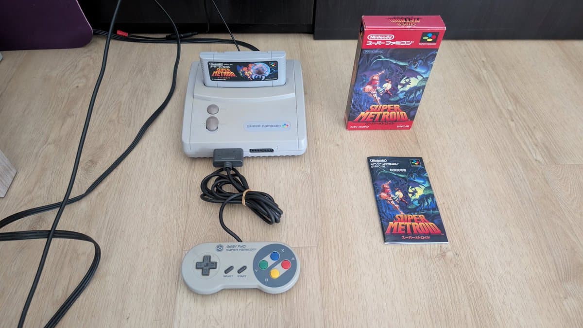 Super Famicom Jr. console with controller, power cable, and Super Metroid game boxes displayed on wooden desk surface.