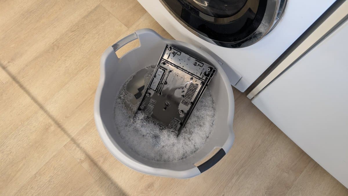Sega Master System MK-2000 circuit board soaking in soapy water in a basin for cleaning during refurbishment.