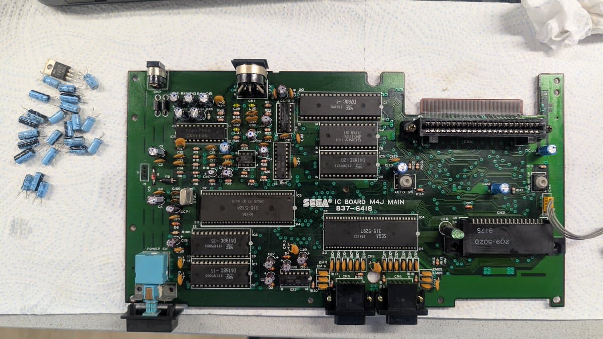 Sega Master System M4J main board with removed capacitors displayed left, showing refurbishment work including component replacement and cleaning.