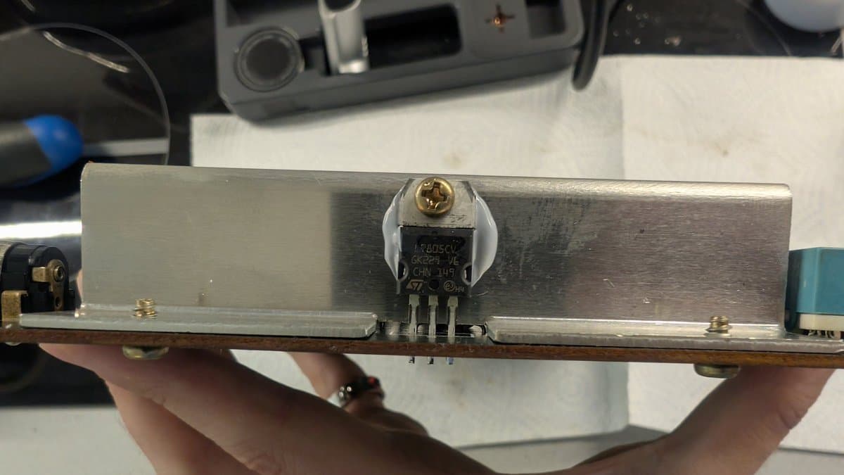 Close-up of Master System motherboard showing replaced voltage regulator IC with thermal paste application and cleaned solder joints during refurbishment.