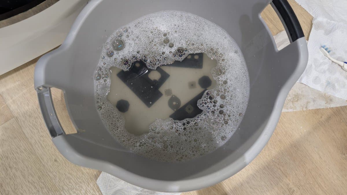Electronic components soaking in soapy water in a basin during Master System controller cleaning and refurbishment.