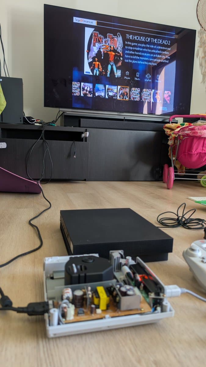Dreamcast VA0 console displaying Sonic Adventure during burn-in test, with power supply and controller visible on wooden desk.