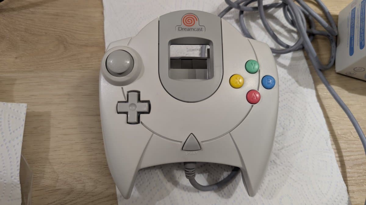 Refurbished Dreamcast controller showing clean white casing, analog stick, d-pad, four colored action buttons, and cable after cleaning restoration.