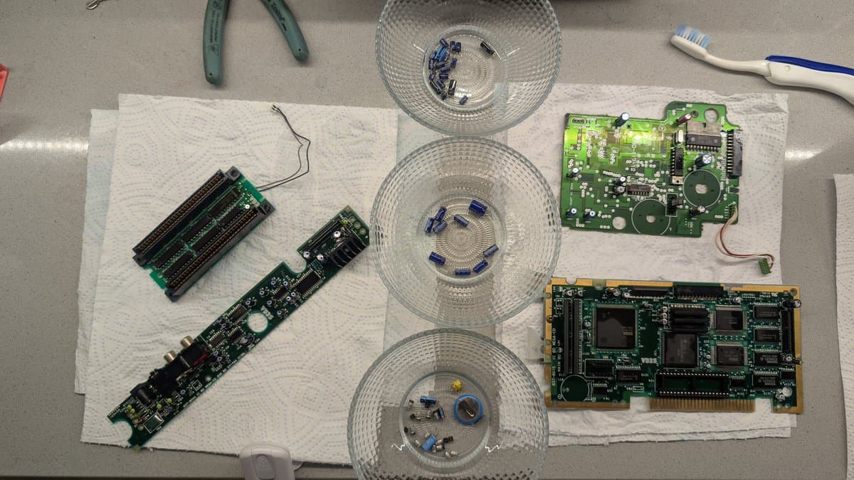 Mega-CD 1 boards post-ultrasonic cleaning: three circuit boards on paper towels, three clear containers with optical components, tools and toothbrushes nearby.