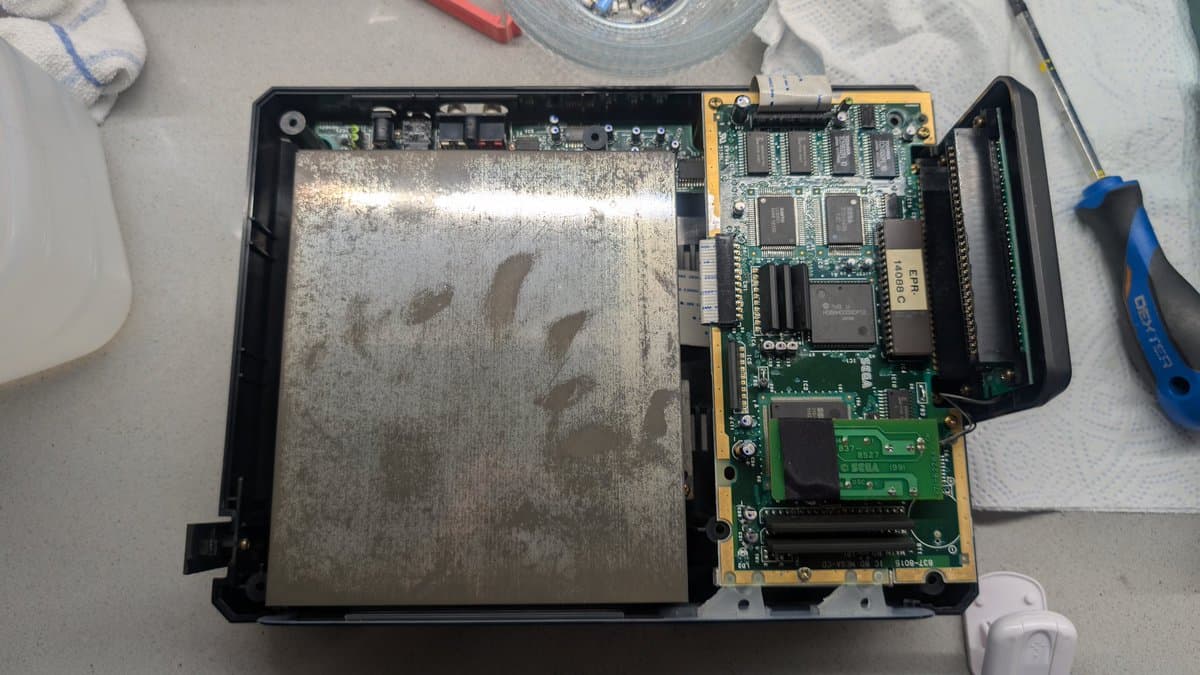 Sega Mega-CD 1 interior disassembled showing large metallic shielding, circuit boards with IC chips, and yellow/green PCBs during restoration diagnostics.