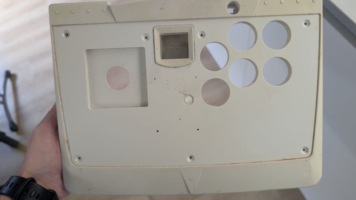 Dreamcast arcade stick bottom panel showing yellowed plastic casing, circular button openings, and rectangular screen area with visible discoloration and wear.