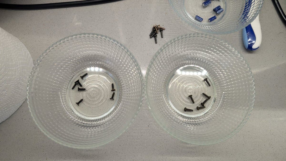 Two clear petri dishes containing Dreamcast metal parts soaking in Evaporust solution, with screws visible in circular rust removal treatment.