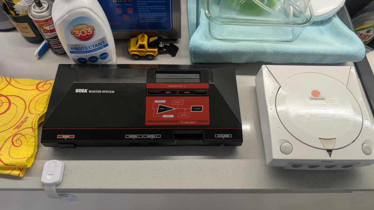 Refurbished Master System MK-2000 on desk with 303 protectant, isopropyl alcohol, microfiber cloth, and Dreamcast console nearby before final sendoff.