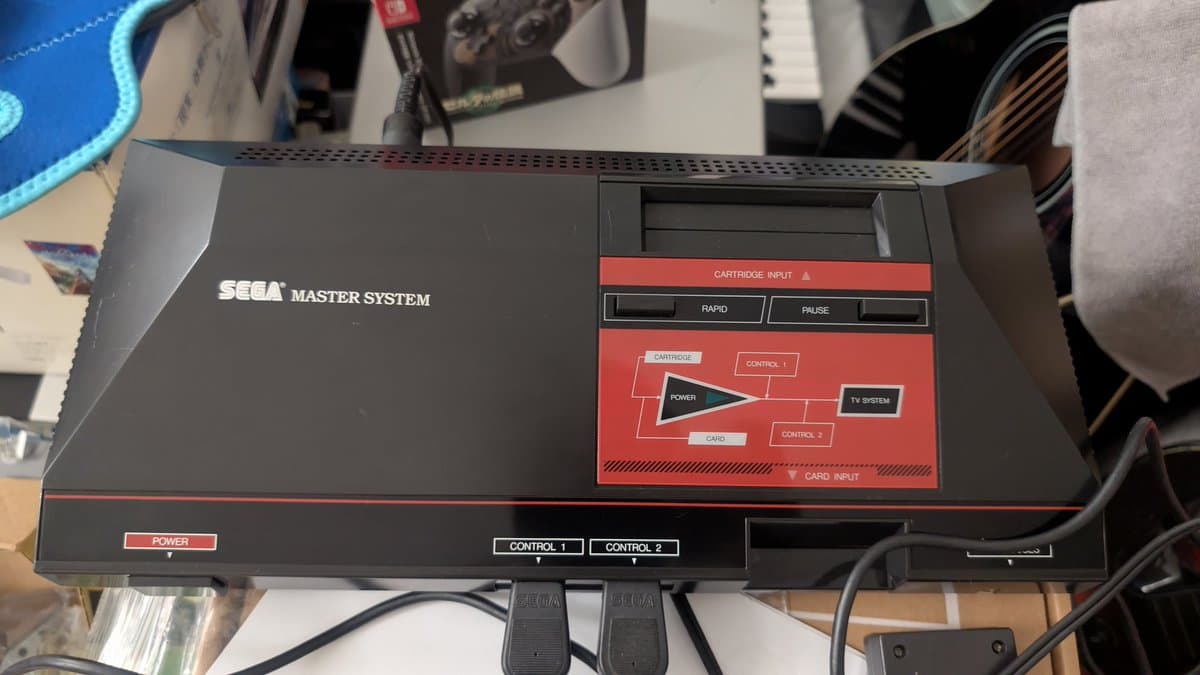 Sega Master System console top view showing cartridge input and control ports with documentation diagram visible on red label.