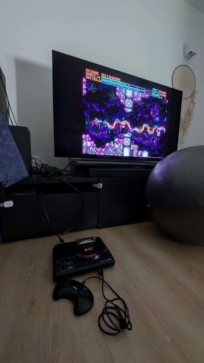 Sega Mega Drive console displaying Earthion gameplay on TV, with 16-bit controller and console unit visible on wooden desk during final testing.
