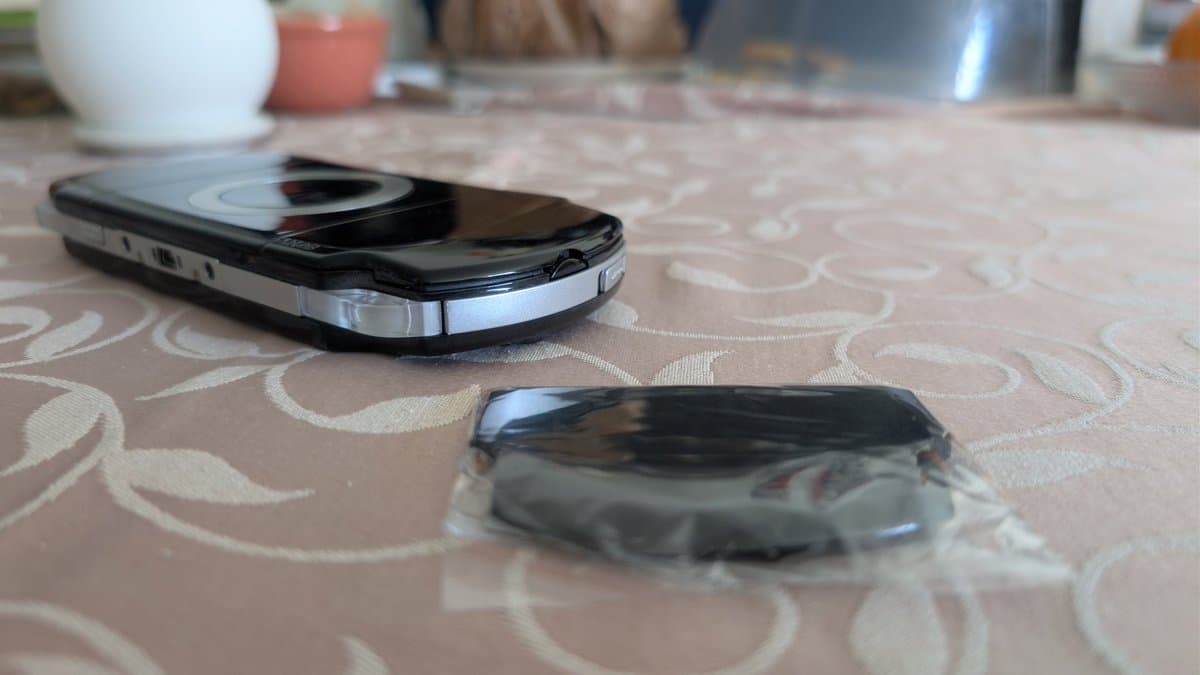 Two PSP devices on patterned fabric; upper unit shows swollen battery with broken battery door retaining clip; lower unit displays battery damage.