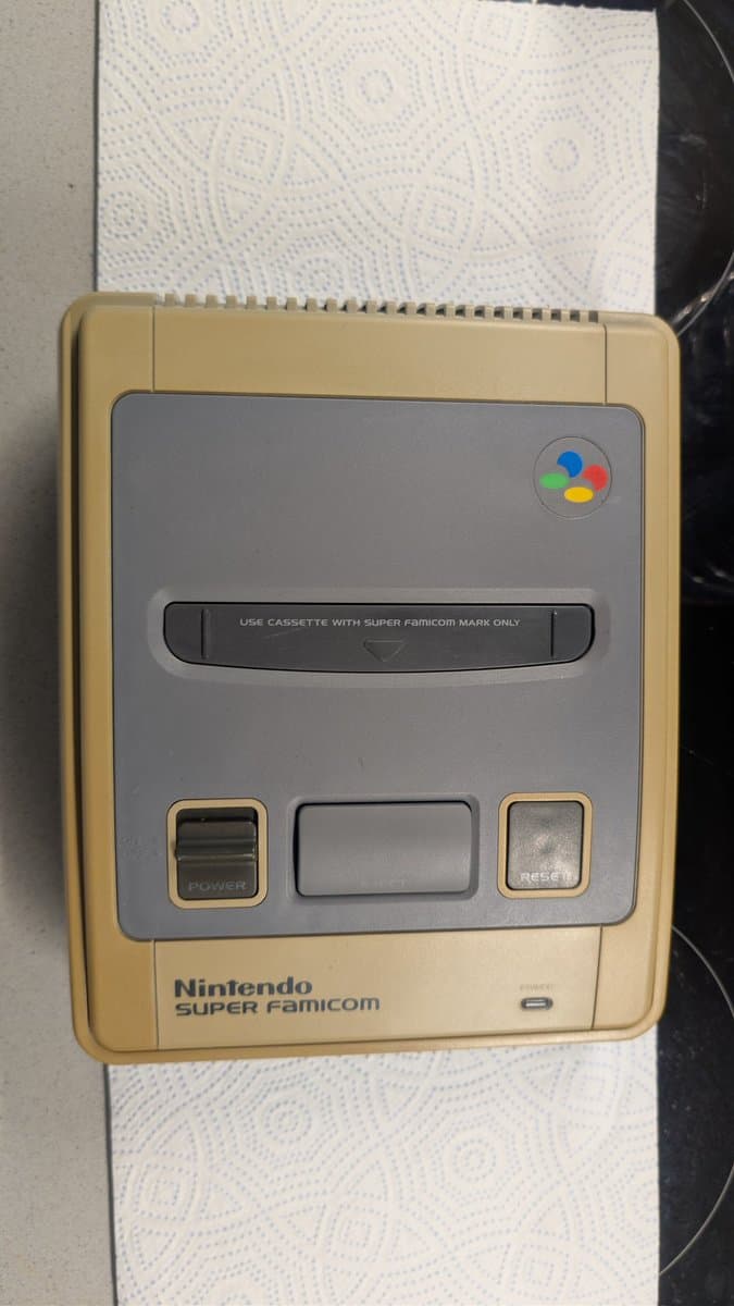 Yellowed Nintendo Super Famicom console showing discolored tan shell with gray faceplate, cassette slot, and control buttons before restoration work.