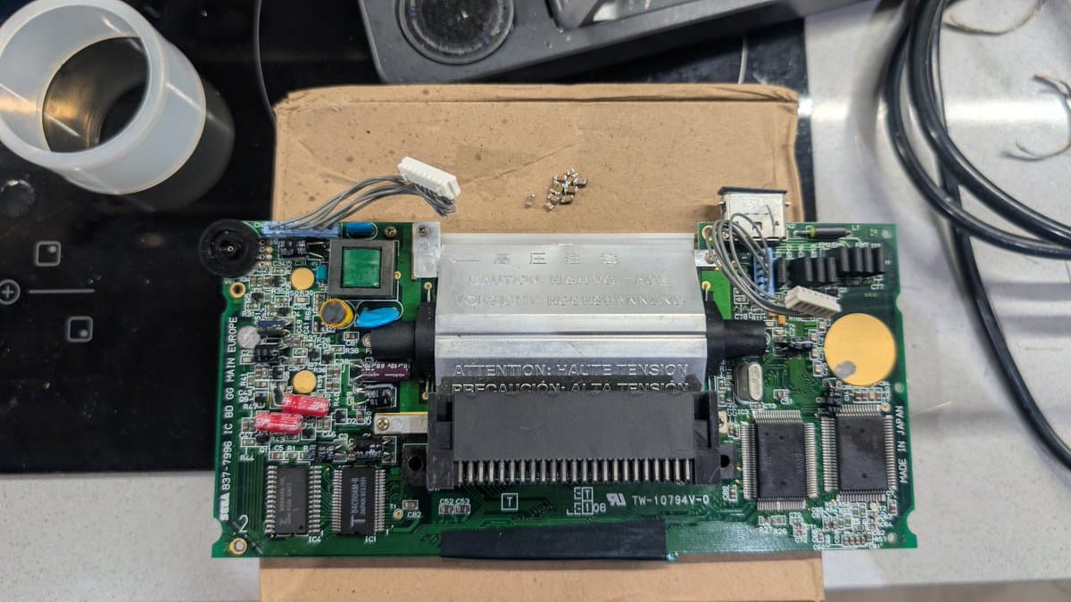 Game Gear mainboard with ceramic capacitors replaced by electrolytic capacitors during recap repair, showing exposed PCB and component areas.