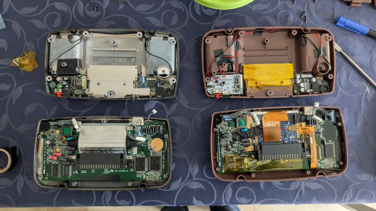 Four Game Gear motherboards displayed during recap and mod transfer work, showing exposed PCBs, capacitors, and internal components at various stages of disassembly.