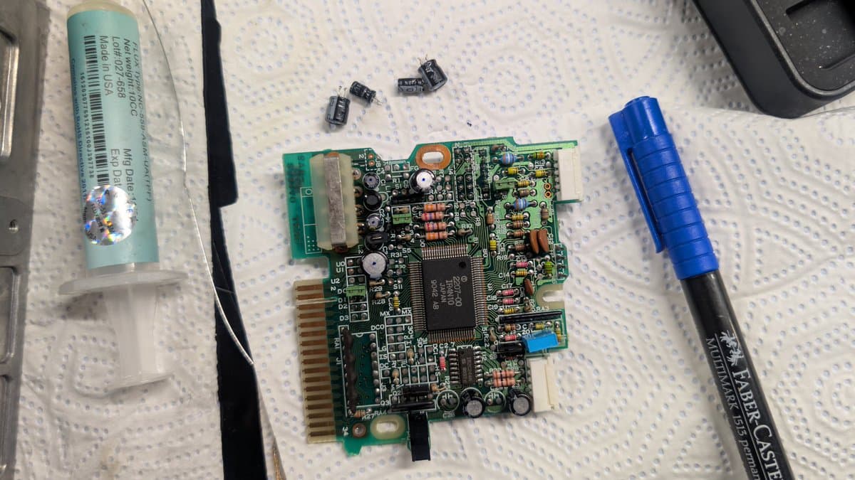 Recapped X68000 Pro II board with removed electrolytic capacitors, flux pen, and desoldering tool on work surface.