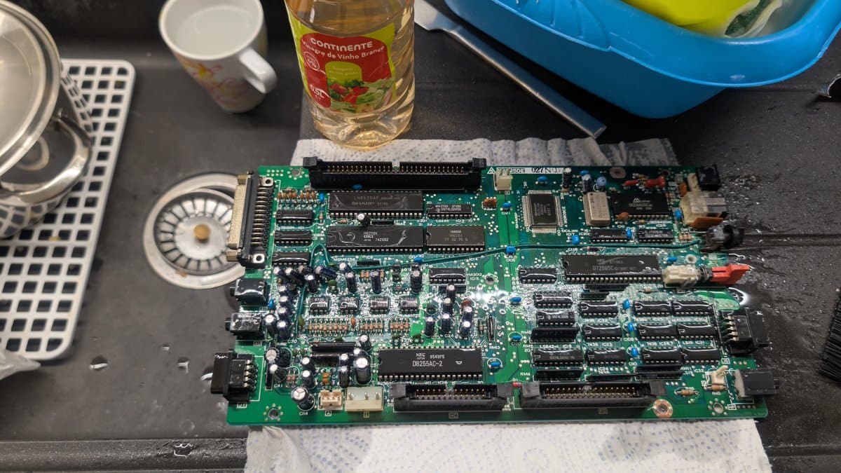 Sharp X68000 lower board being cleaned with white vinegar to neutralize electrolytic fluid damage, surrounded by IPA and repair supplies.