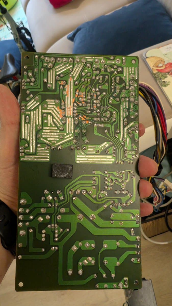 PSU PCB held in hand showing failed capacitors with oxidized solder joints and corroded component leads after ultrasonic cleaning.
