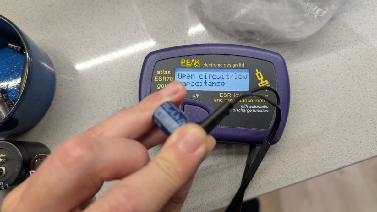PEAK ESR70 meter displaying "open circuit/low capacitance" while testing PSU capacitor with probe, indicating failed component.