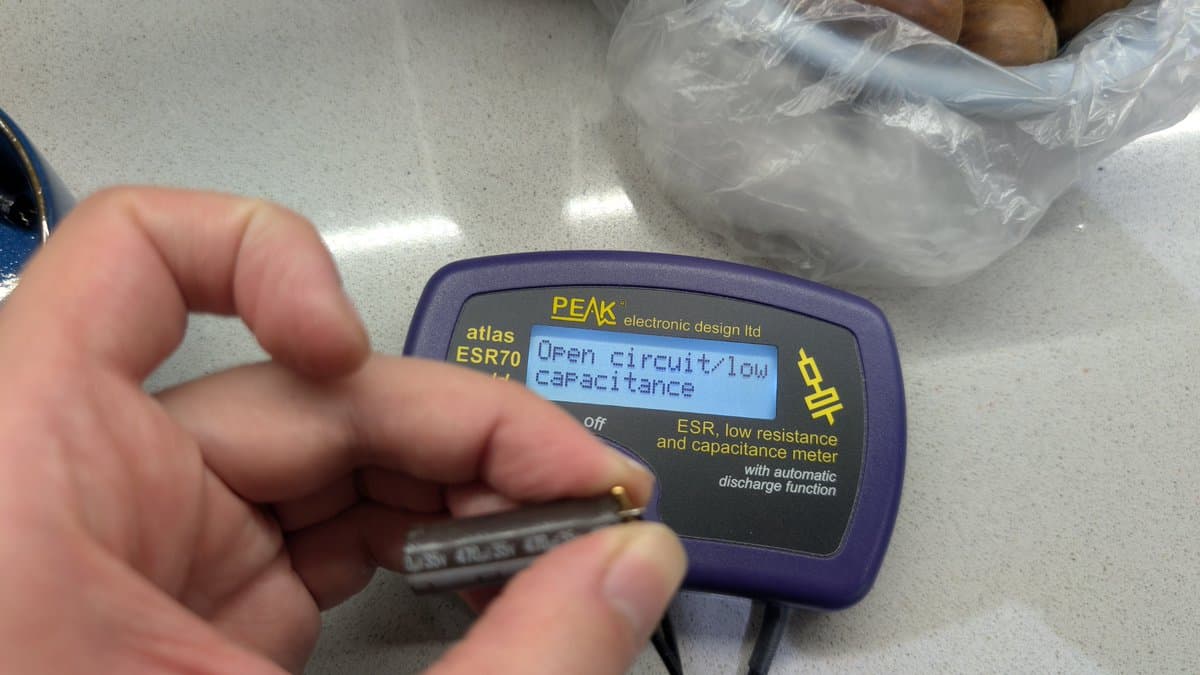 Close-up of PEAK Atlas ESR70 meter showing "Open circuit/low capacitance" reading during Sharp X68000 PSU capacitor testing.