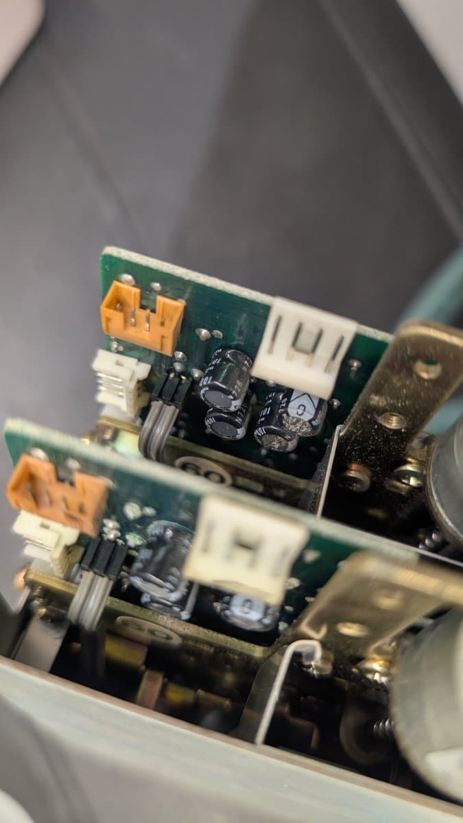 Two stacked green PCBs with orange connectors showing internal components; upper board has 4 capacitors, lower has 3, displaying capacitor damage aftermath.
