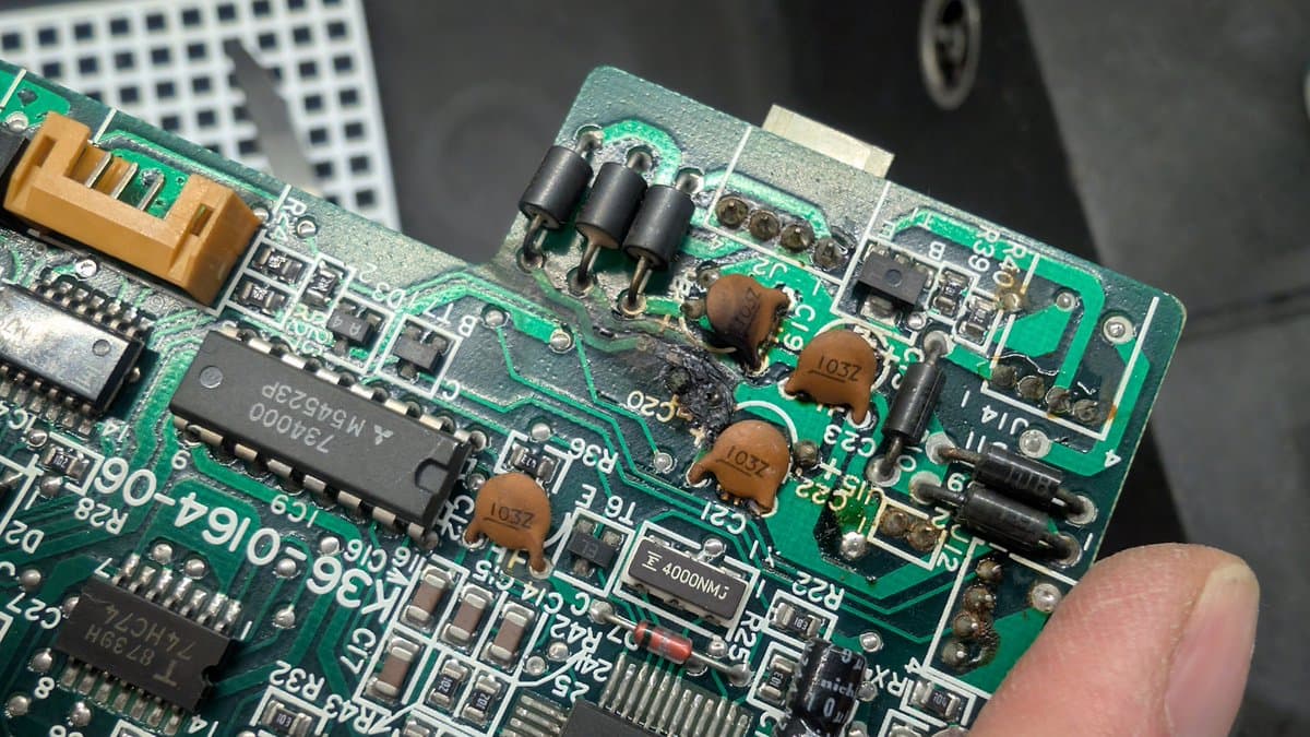 Leaking capacitor damage on Sharp X68000 PCB; burnt component area, discolored traces, and adjacent resistors showing thermal stress from failed capacitor.