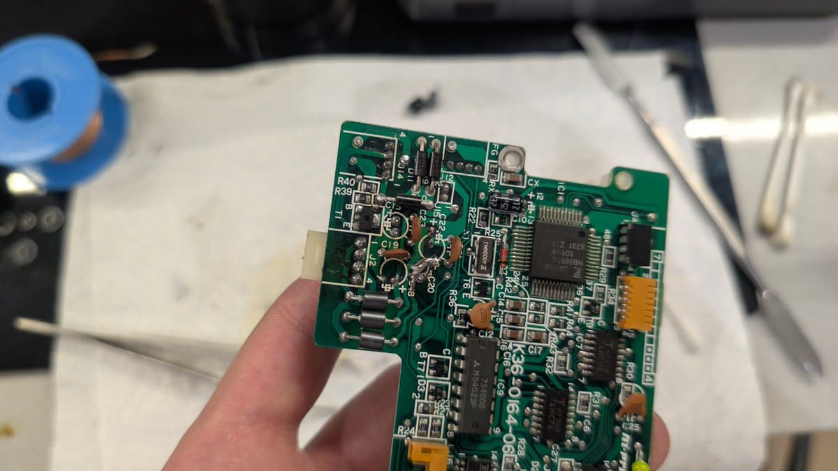 Close-up of Sharp X68000 circuit board being held, showing recapped capacitors, IC chips, and component-level repair work in progress.