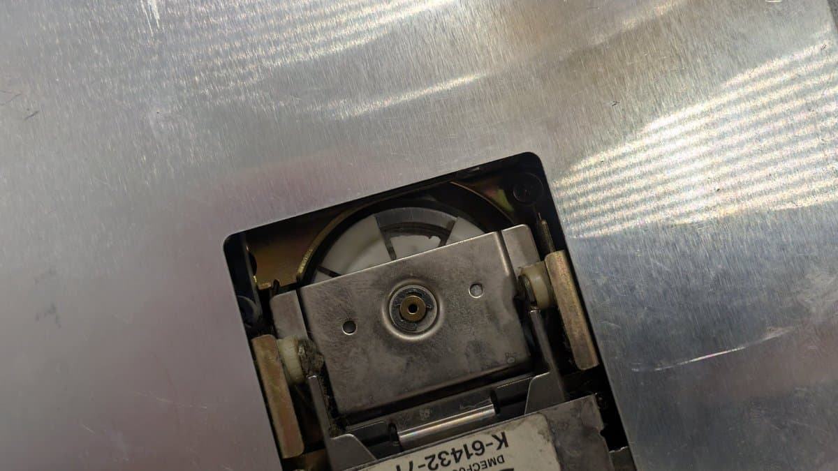 Sharp X68000 FDD spindle mechanism with broken piece lodged underneath, magnetic disk debris visible during restoration.