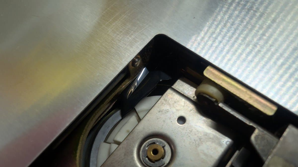 Sharp X68000 floppy drive spindle mechanism with broken plastic piece lodged underneath, magnetic disk debris visible.